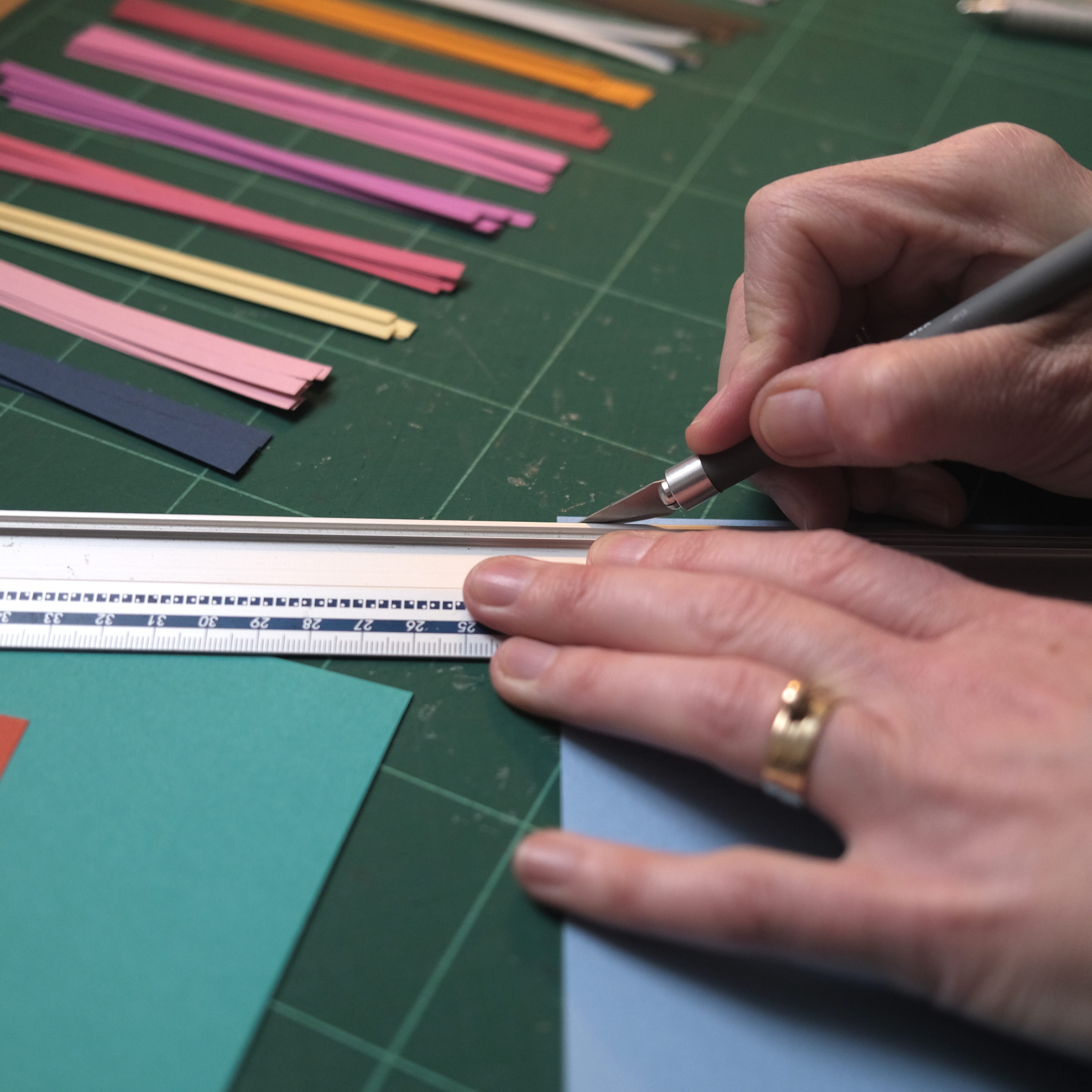 hand holding scalpel, cutting paper against a ruler